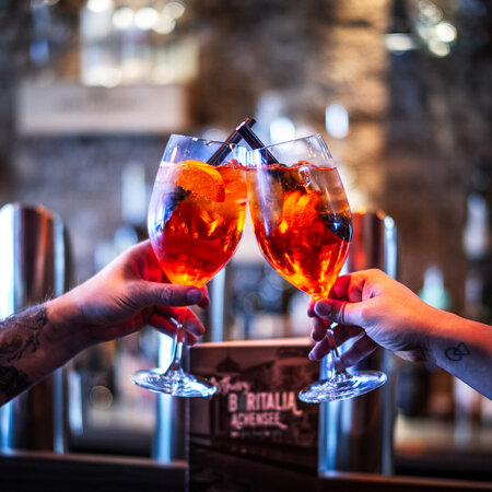 Two people clinking Aperol Spritz glasses in a stylish bar atmosphere