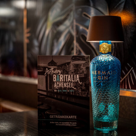 Gin bottle with mini lamp beside menu on a dark table