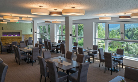 Heller Speisesaal mit großen Fenstern und Blick auf Bäume und Berge im Hintergrund