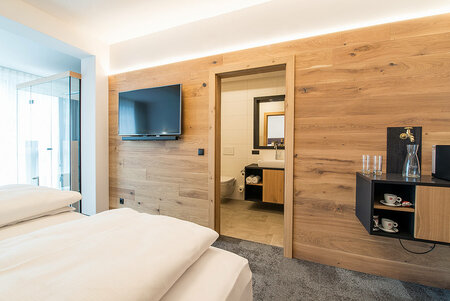 View from hotel room into modern bathroom with wood accents, vanity and lit mirror