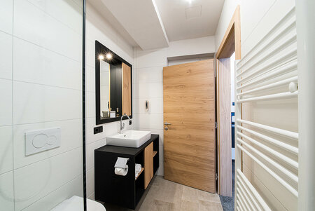 Bright hotel bathroom with wooden door, towel warmer, WC and modern white and black design