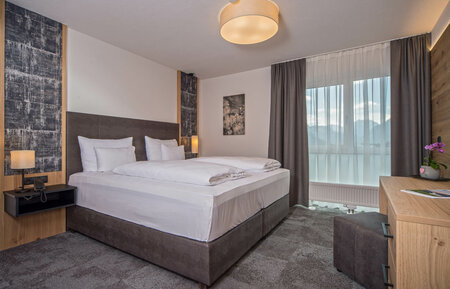 Modern double room with cozy bed, desk and mountain view through large bright windows