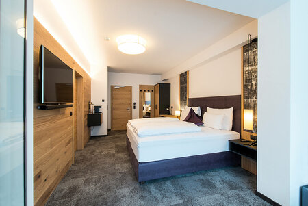 Spacious hotel room with double bed, TV, coffee station and cozy wooden wall cladding