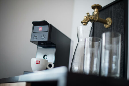 Modern Illy coffee machine with cup, glass carafe and glasses next to decorative water tap